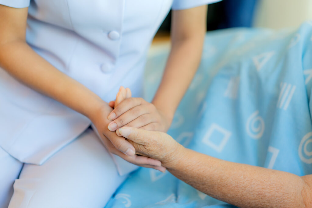 Nurse sitting on a hospital bed next to an older woman helping hands, care for the elderly concept